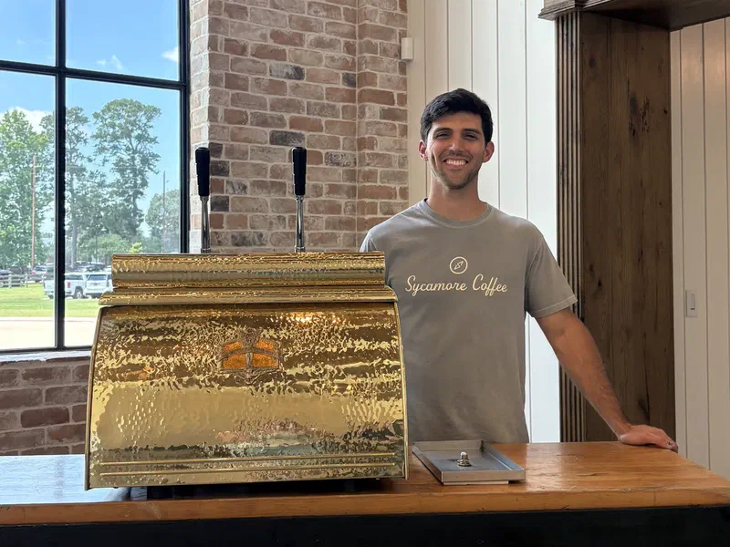 A barista behind the Sycamore coffee cart and its brass espresso machine